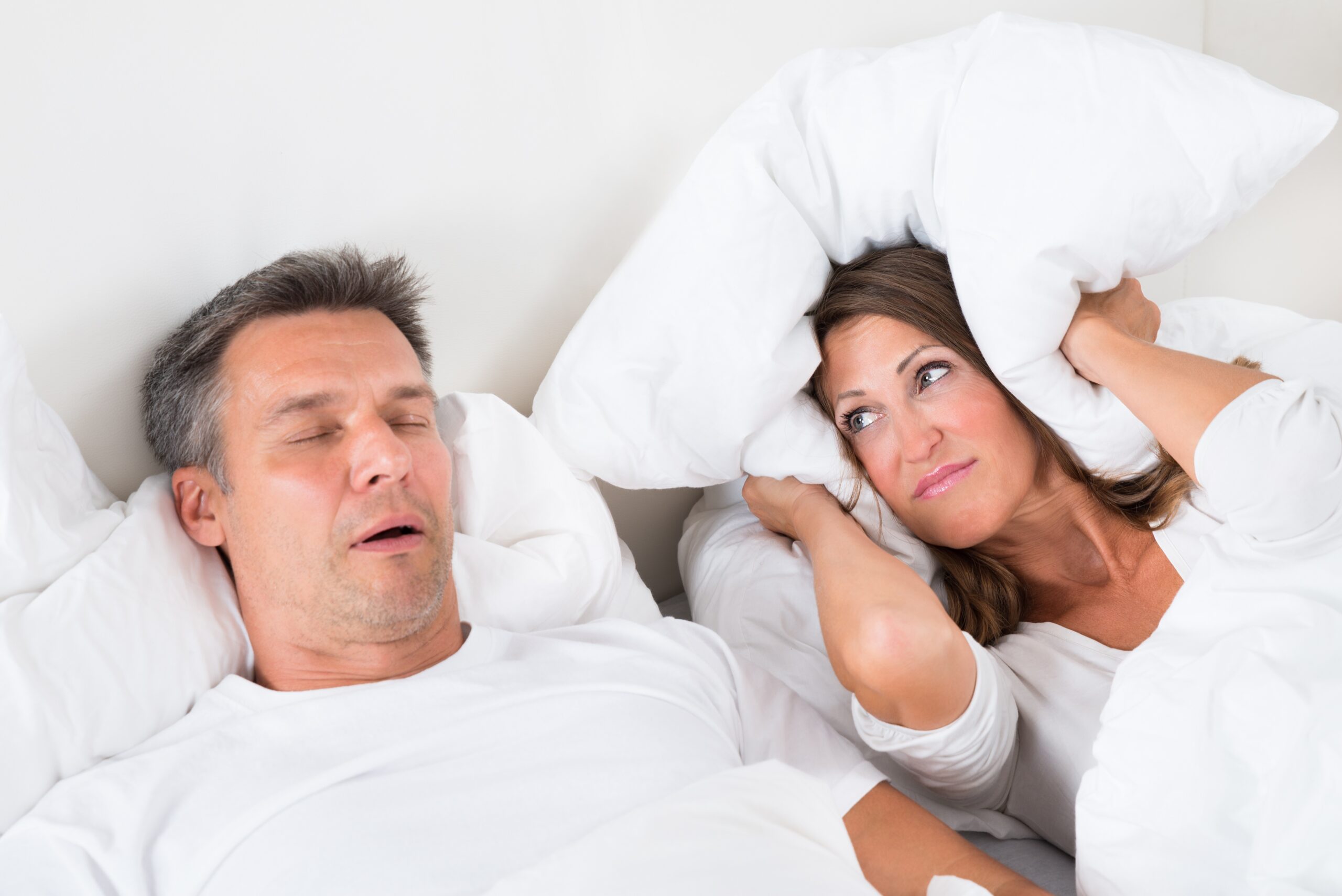 A husband snoring in bed next to his wife.
